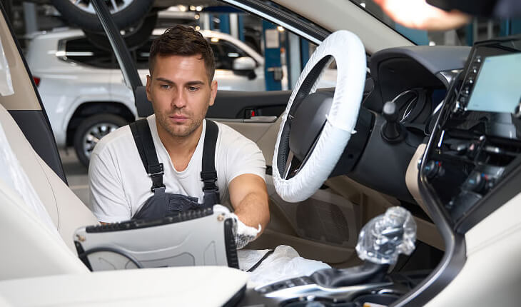A man repairs a car in a garage, surrounded by tools and equipment, focused on his work.