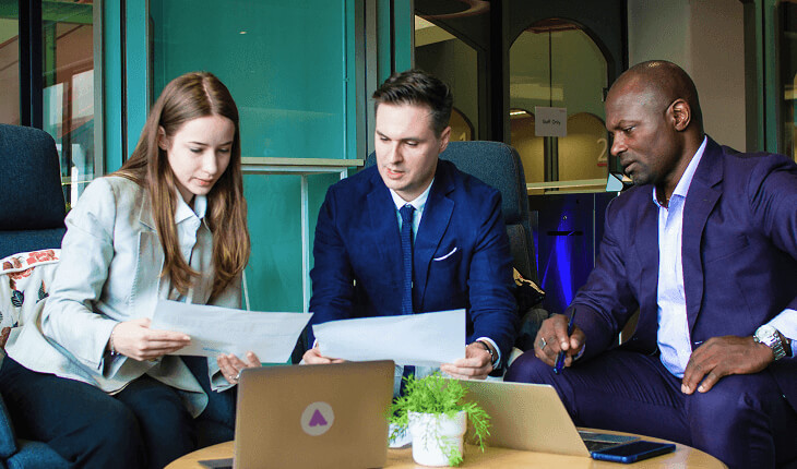 Three business professionals seated at a table, reviewing documents and discussing strategies.
