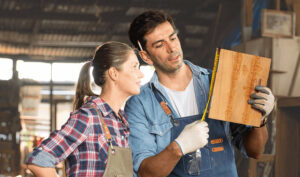 A man and woman in overalls examine a piece of wood together, discussing its features and potential uses.